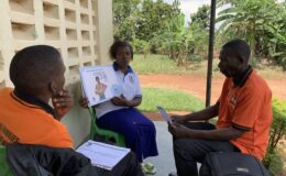 A VHT shows a YBU team member how she uses the flip chart at a sensitisation meeting